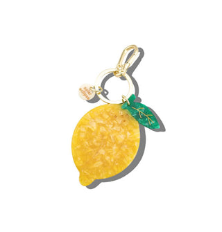 Quartz-like acetate yellow lemon with green leaf and stem hangs from a gold keyring with tab and lobster clasp attached