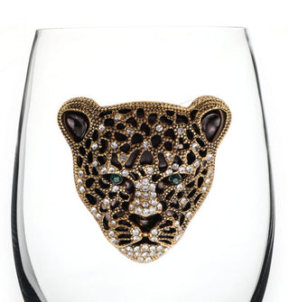 Closeup of an enameled leopard face insignia with gold edging, accented with clear rhinestones all over and green rhinestones for its eyes, on the bowl of a clear wine glass