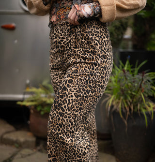 Model tugs at the waist of a pair of leopard print pants