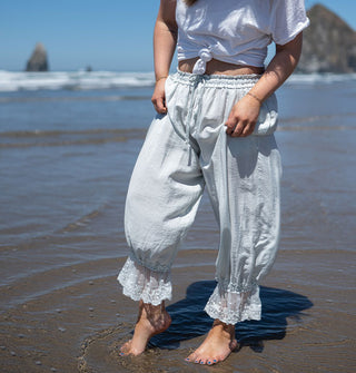 Model standing in shallow ocean water at the beach wears nearly white, light blue, lace-trimmed pantaloons with a white T-shirt