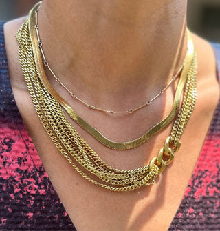 Model wears a gold-toned necklace with multiple strands of narrow curb chain on either side connected by three large curb links off-center to the right paired with two other gold-toned chain necklaces