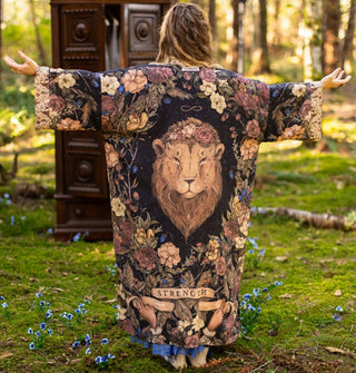 Model facing away from camera with arms outstretched wears a floral print robe with central lion's head on the back, under which is a banner that reads, "Strength"