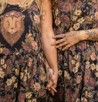 Two models holding hands each wear a floral patterned dress, one with a lion's head on the bodice