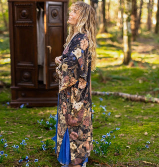 Model standing in a mossy forest with a wardrobe in the background wears a floral print robe over a bright blue dress