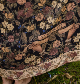 Skirt fabric featuring a floral print accented with two Victorian-style hands holding a banner that says, "Strength" above a contrasting printed hem border
