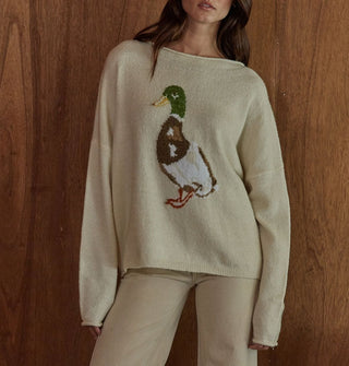 Model standing against a woodgrain backdrop wears a cream-colored sweater with mallard graphic