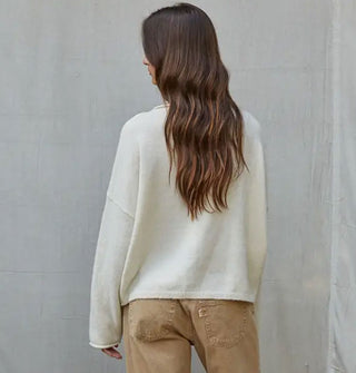 Model facing away from the camera wears a white sweater with tan pants