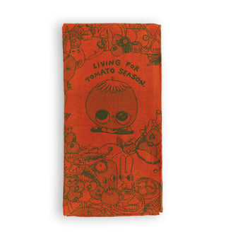 Reddish-orange dish towel features whimsical illustrations at the center of which is a wide-eyed tomato appearing to gaze up at the words, "Living for tomato season."