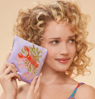 Smiling model holds a lavender embroidered lobster pouch up to face