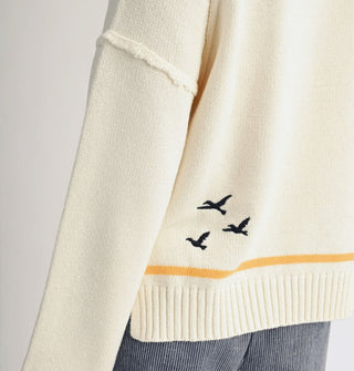 Silhouettes of three seagulls in flight on the back of a cream-colored sweater with yellow stripe along the bottom ribbed hemline