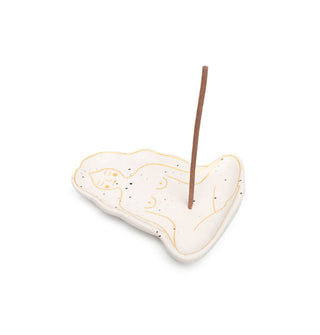 Flecked white ceramic incense dish decorated with metallic gold outline illustration of a naked woman seated in lotus pose, an incense stick emerging from where her belly button would be