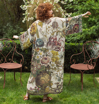 Model standing in a garden with arms outstretched wears a long robe with floral design contrasted by bumblebee print edges