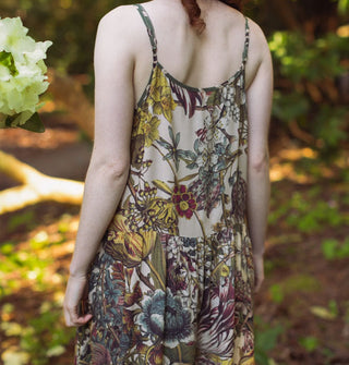 Model in a forest setting wears a lushly floral patterned slip dress