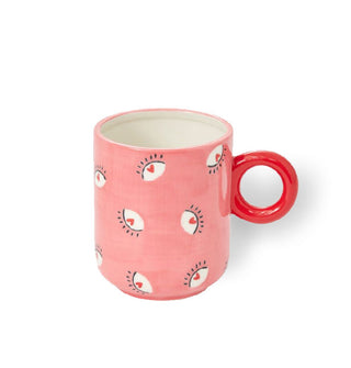 Pink coffee mug with round red handle features an all-over design of stylized eyes with hearts in their centers