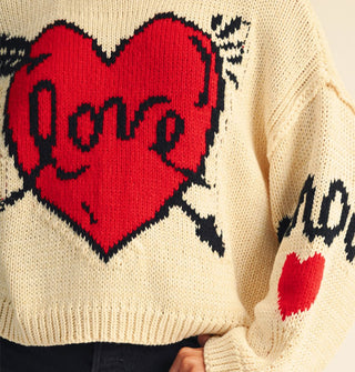 Cream-colored sweater with graphic arrow-pierced red "Love" heart design and "Amour" on the sleeve above another red heart