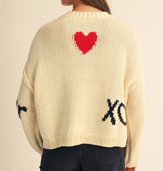 Back of a cream-colored sweater features a red heart near the top and "XO" in black near the bottom at right