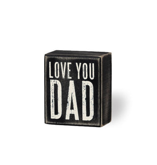 Rectangular black distressed wood box sign says, "Love you dad" in large white uppercase letteirng
