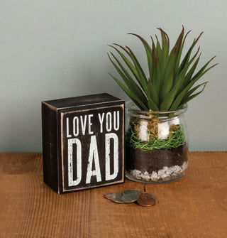 Black and white wooden "Love you dad" box sign s staged with a jarred succulent and loose change on a rustic wooden tabletop