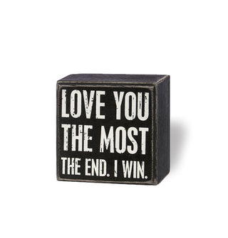 Square black box sign with distressed finish says, "Love you the most" in large white lettering and, "The end. I win" underneath in smaller white lettering