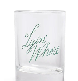 Clear shot glass says, "Lyin' Whore" in green script lettering set at a tilt