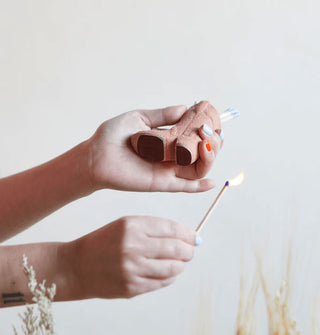 Model strikes a wooden matchstick on the bottom of a cowboy boot-shaped match holder