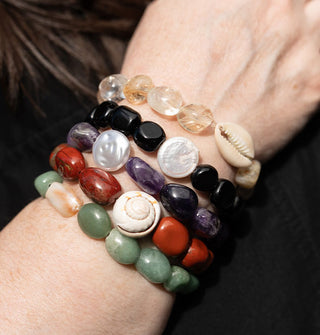 Closeup of model's wrist wearing five stone bracelets, some with seashell accents