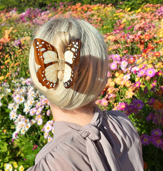 Model standing in front of a flower patch wears a brown and white monarch butterfly hair clip in a twisted-up style