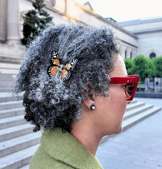 Model wears an orange monarch butterfly hair clip at the side of her head
