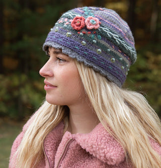 Model in pink fleece wears a blue and gray striped wool beanie with a scalloped edge and textural embroidered flowers, vines, and polkadots
