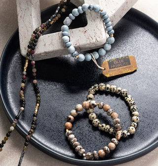 One blue howlite and two dalmatian jasper stone bead bracelets rest on a stoneware dish with two strands of smaller dark beads