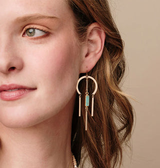Model wears a gold earring with a rounded top and turquoise stone center dangle