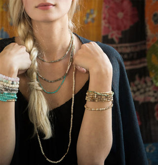 Model wears a collection of beaded stone necklaces and bracelets