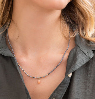 Model wears a thin beaded necklace with teardrop charm
