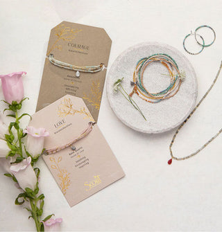 A collection of beaded stone jewelry staged with purple flowers