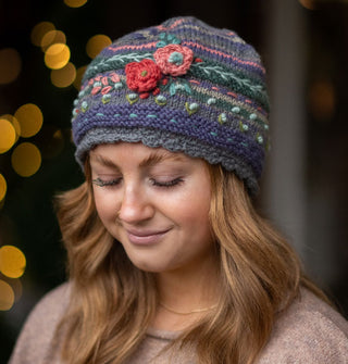 Smiling model wears a colorful knit beanie with textural floral, vine, and polka dot embroidery