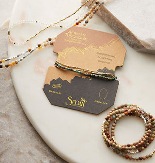 Beaded jewelry on a stone surface with one African Turquoise bracelet/necklace piece wrapped around its product card