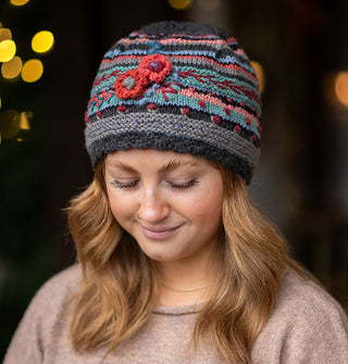 Smiling model wears a colorful knit beanie with textural floral, vine, and polka dot embroidery