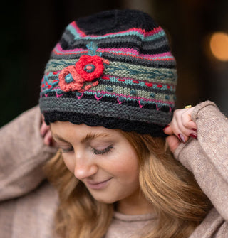 Smiling model puts on a colorful knit beanie with textural floral, vine, and polka dot embroidery