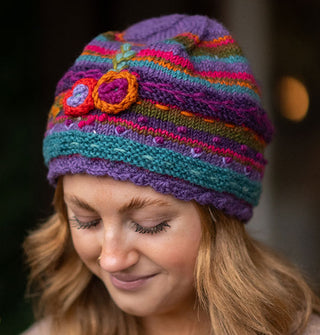 Smiling model wears a colorful knit beanie with textural floral, vine, and polka dot embroidery