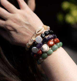 Closeup of model's wrist wearing five stone bracelets, some with seashell accents