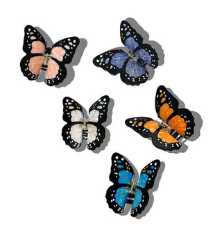 Five monarch butterfly hair clips, one white, one dark periwinkle blue, one orange, one pink, and one lighter cerulean blue, all with black wing borders with white spots