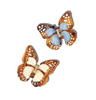 Two monarch butterfly hair clips, one with cream-colored wing centers and one with baby blue, both with streaked brown edges accented with white speckles