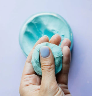 Model presses their thumb into a ball of blue Pinch Me Therapy Dough