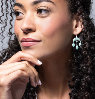 Model wears a dangle earring with three rounded diamond-shaped turquoise stones attached to an upper cresent-shaped turquoise stone