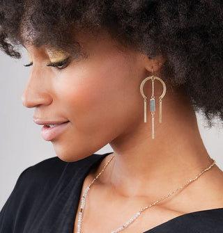Model wears a gold earring with a rounded top and labradorite stone center dangle