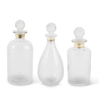 Three faceted glass decanters in different shapes and graduated sizes, each with a gold band around the neck and a rounded stopper in the opening