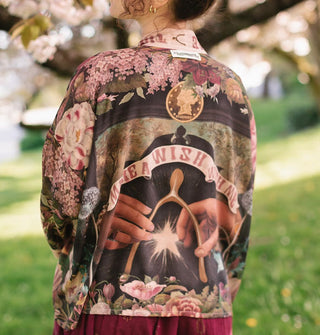 Model wears a cropped silken robe with pink florals and a wishbone design with hands and a star on the back below a text banner that says, "Make a wish with me"