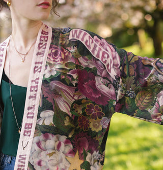 Model wears a lush pink and purple floral print robe with contrasting text banner trim and a banner that reads, "Wishes" on the shoulder