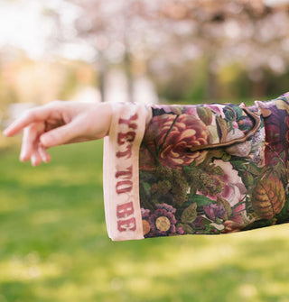 Model's outstretched arm wears a loose-fitting sleeve with pink and purple florals and a text banner trim that says, "yet to be"