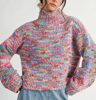 Model with hands on hips wears a multicolored, oversized  turtleneck sweater